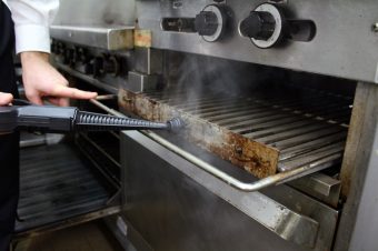Duplex commercial steam cleaner being used to clean an oven in a commercial kitchen.