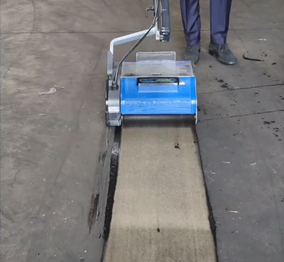 Duplex cleaning machine removing heavy dirt from a concrete floor in an industrial setting.