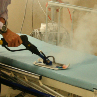 Steam cleaner being used on a hospital bed for surface disinfection and hygiene control.