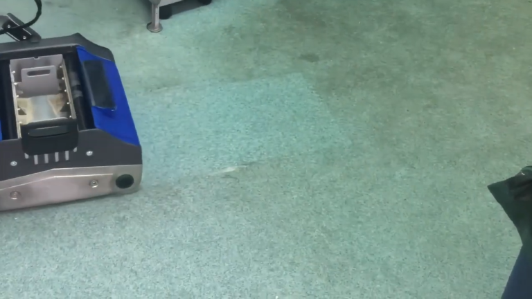 Duplex commercial carpet steam cleaner in action, restoring a heavily soiled carpet floor in an office setting with clear before-and-after results.